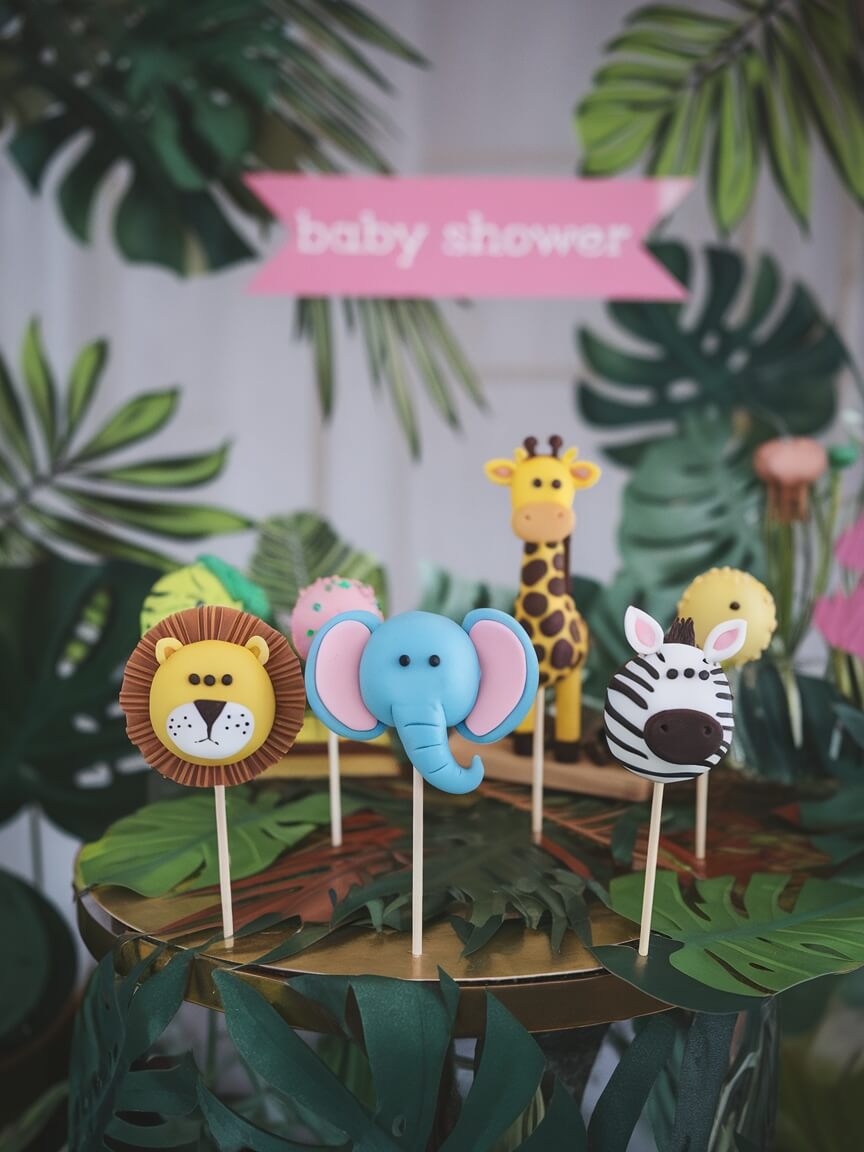 A variety of safari animal cake pops featuring a lion, elephant, giraffe, and zebra, perfect for a jungle themed baby shower.